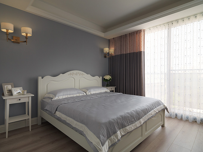 卧室墙面一改蓝色，而是使用了灰色系列，大大的阳台光线十分明亮，而窗帘的选择也是深色遮光的。