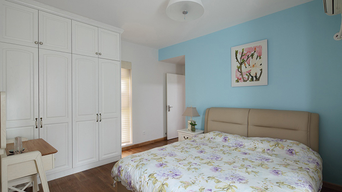 白色的多门壁橱衣柜与白色墙体融为一体突出空间简朴，床头蓝色墙面配搭上一幅兰花增加空间的色彩，简约风格家具与木质结合体现室内舒适。