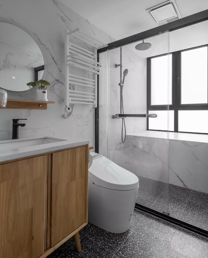 卫生间，黑色水磨石地砖搭配白色仿大理石墙砖，木色的台盆柜注入温暖与自然的格调，玻璃移门隔离淋浴湿区